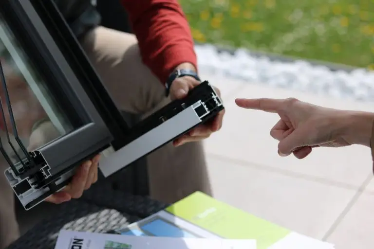 Close-up of two people examining a triple glazed aluminium window frame outdoors.